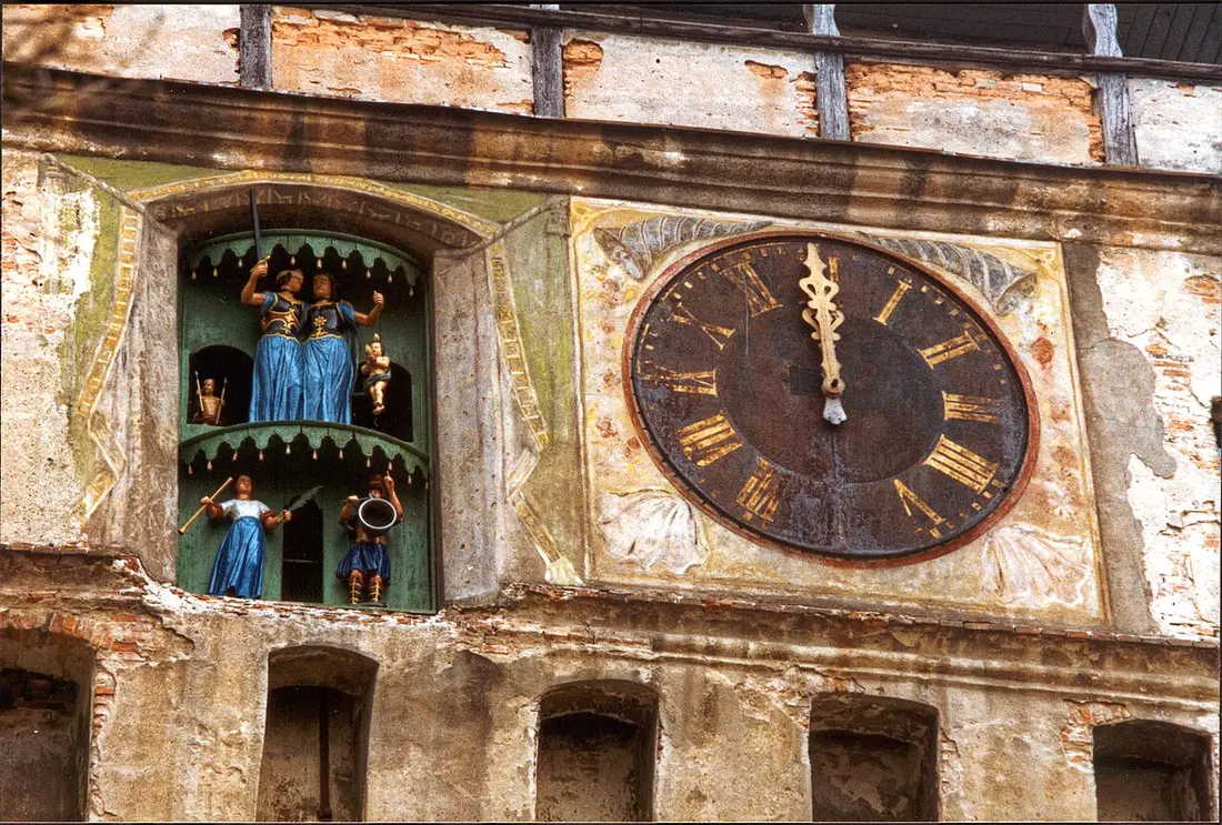 The Clock Tower of Sighisoara, a tall stone tower with a steep tiled baroque roof and clock face, seen from the citadel side