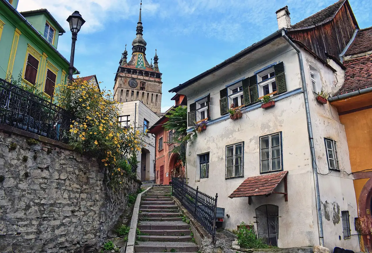 The Sighisoara Clock Tower with its coloured tiled roof rising above pastel houses and a cobbled stairway in the citadel