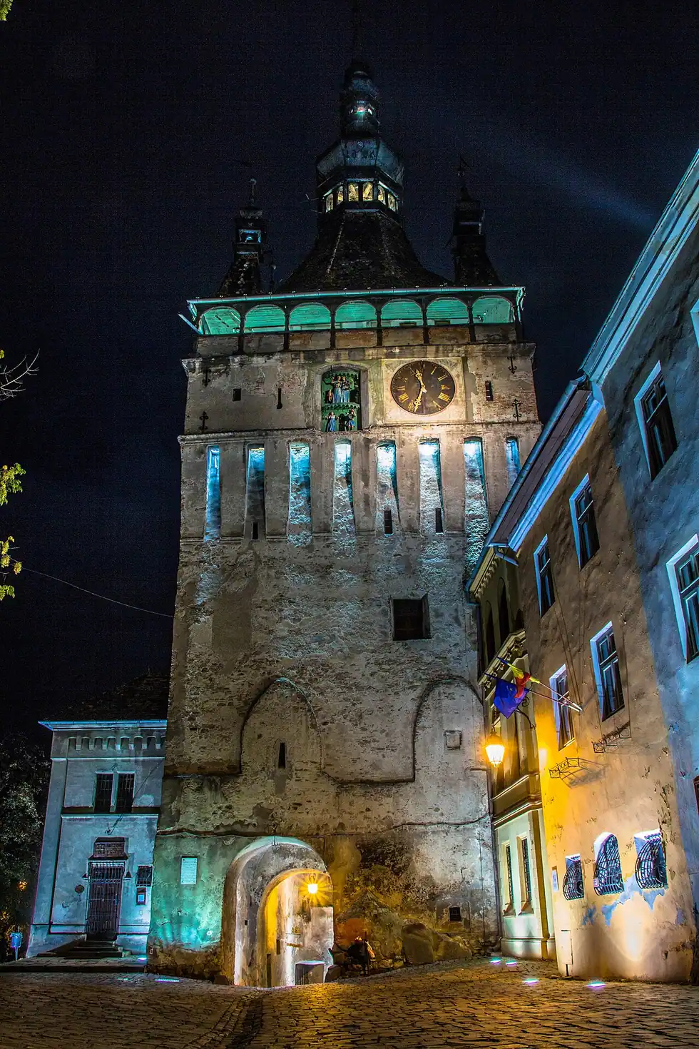 The Sighisoara Clock Tower lit at night above the lantern-lit gate passage into the citadel