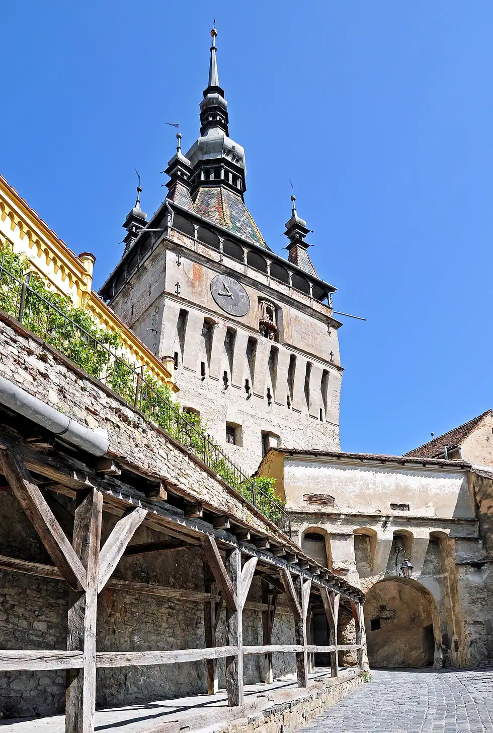 The Sighisoara Clock Tower from the lower town side, showing the clock dial, the figure niche and the covered wooden walkway below