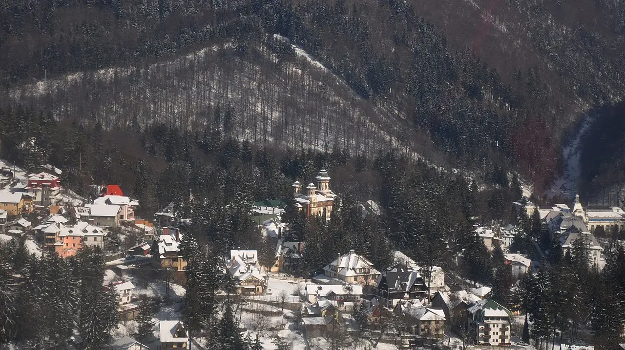 The town of Sinaia under snow, villas and the twin-towered monastery church tucked into a steep forested mountainside in the Prahova Valley