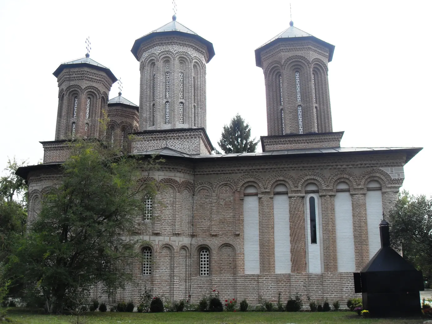 Side view of Snagov Monastery church in exposed brick with four small towers under an overcast sky