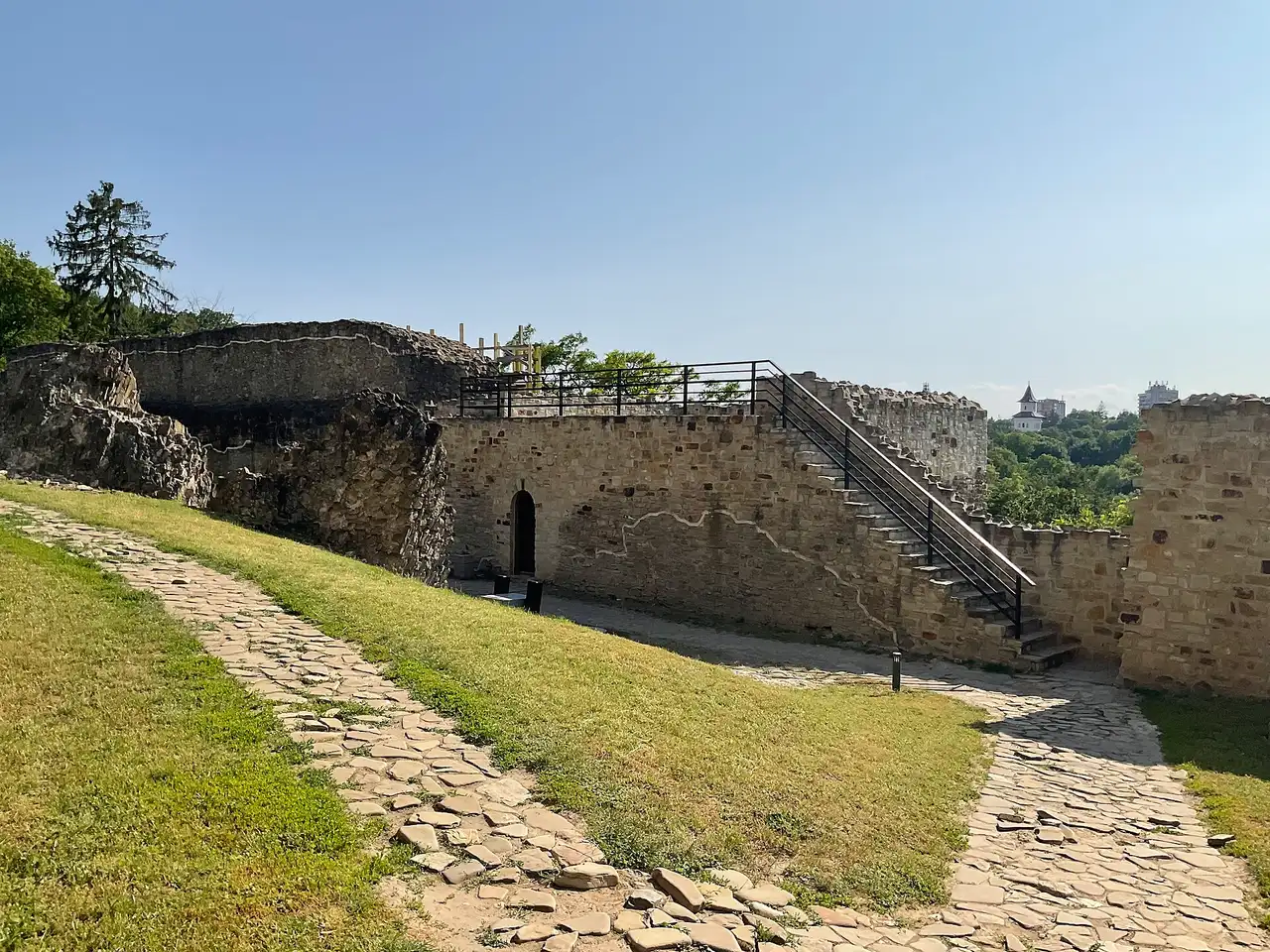 A long stretch of reconstructed stone defensive wall at Suceava Seat Fortress, trees on the hillside behind