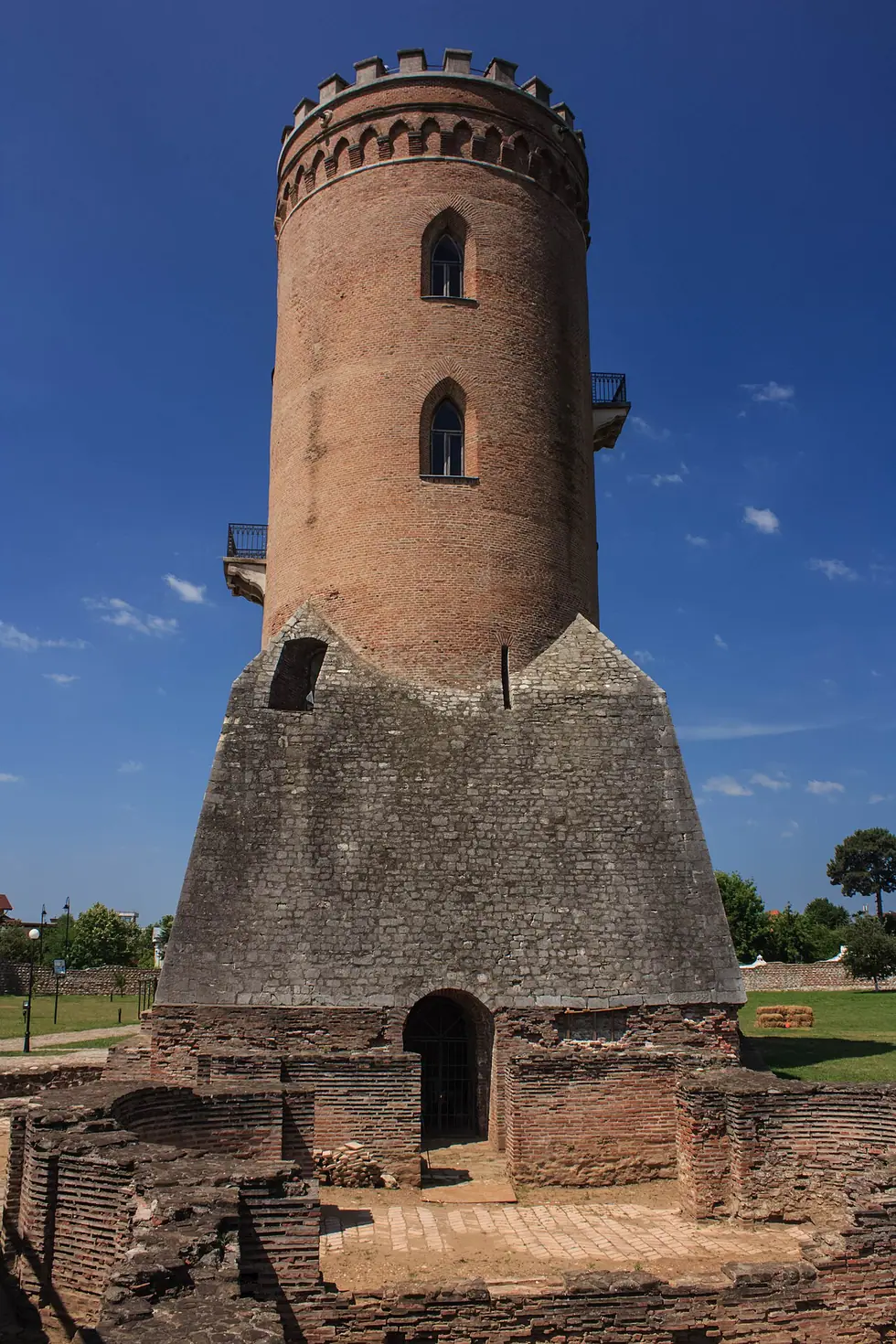 The Chindia Tower rising from its pyramidal stone base above brick ruins at ground level, a doorway visible in the foundation