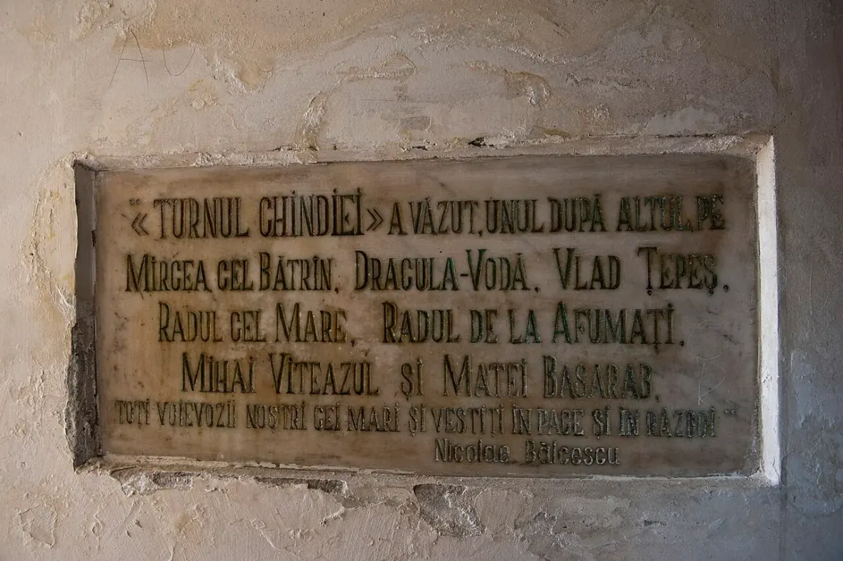 A weathered stone memorial plaque inside the Chindia Tower, engraved with a Romanian inscription by historian Nicolae Balcescu listing the voivodes of Wallachia