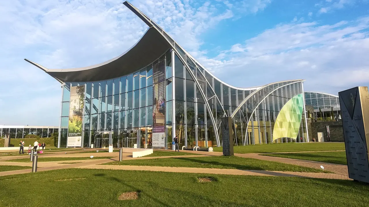 The curved glass and steel exterior of Therme Bucharest at Balotesti under a blue sky