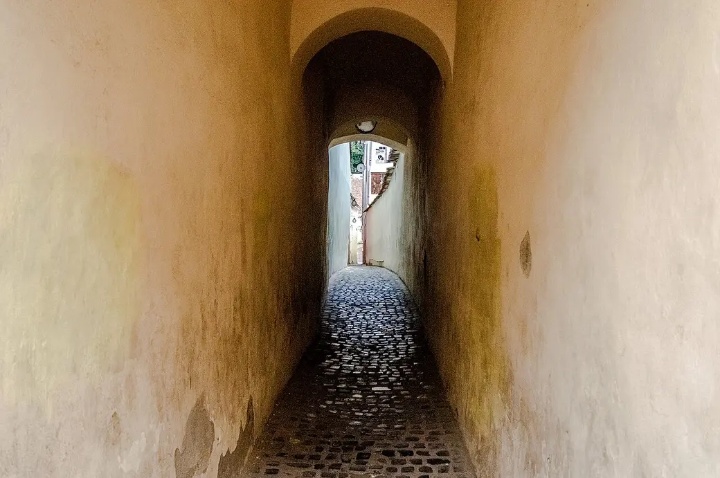 A visitor standing in Rope Street in Brasov with both plastered walls within arm's reach