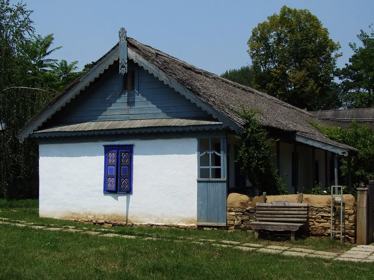 A traditional wooden peasant house with a tall roof at the Village Museum in Bucharest