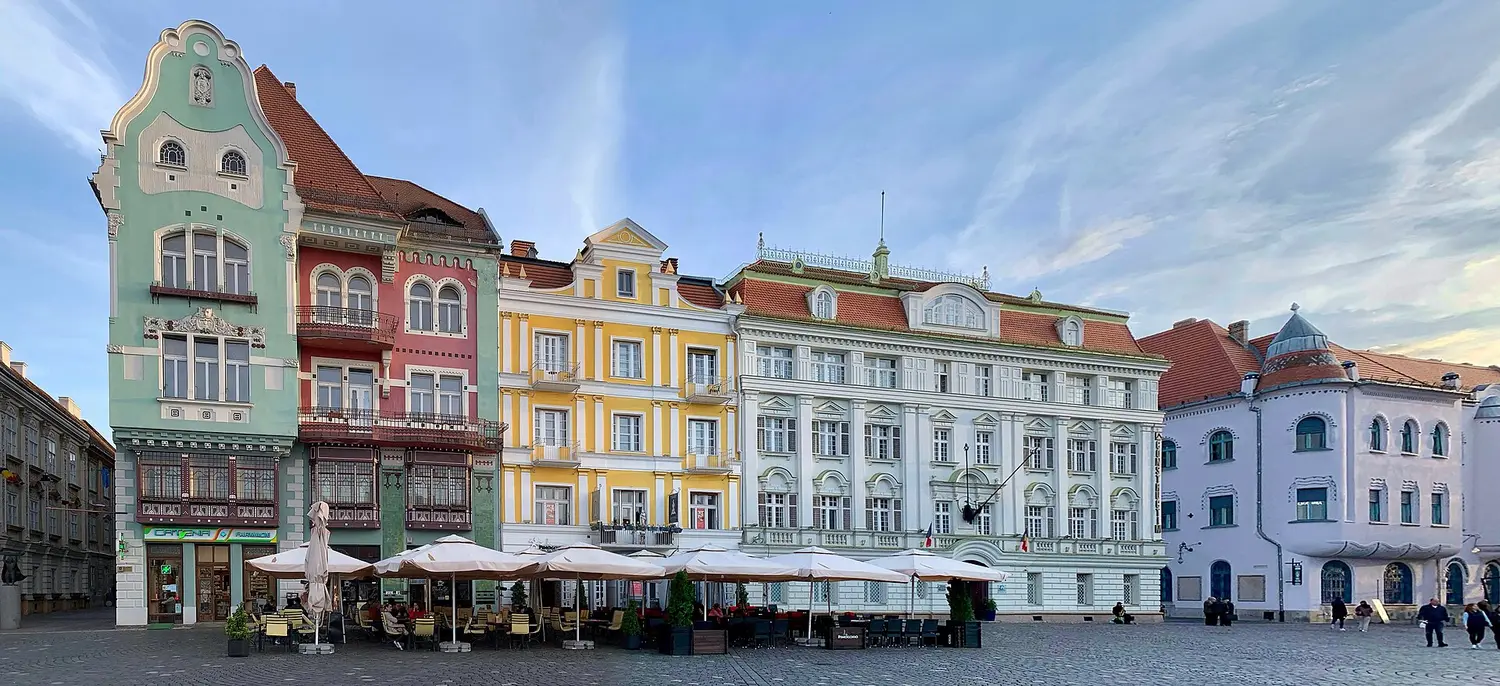 Piata Unirii in Timisoara, a broad Baroque square of restored pink, yellow and green palaces under a blue sky, with the Trinity column in the middle