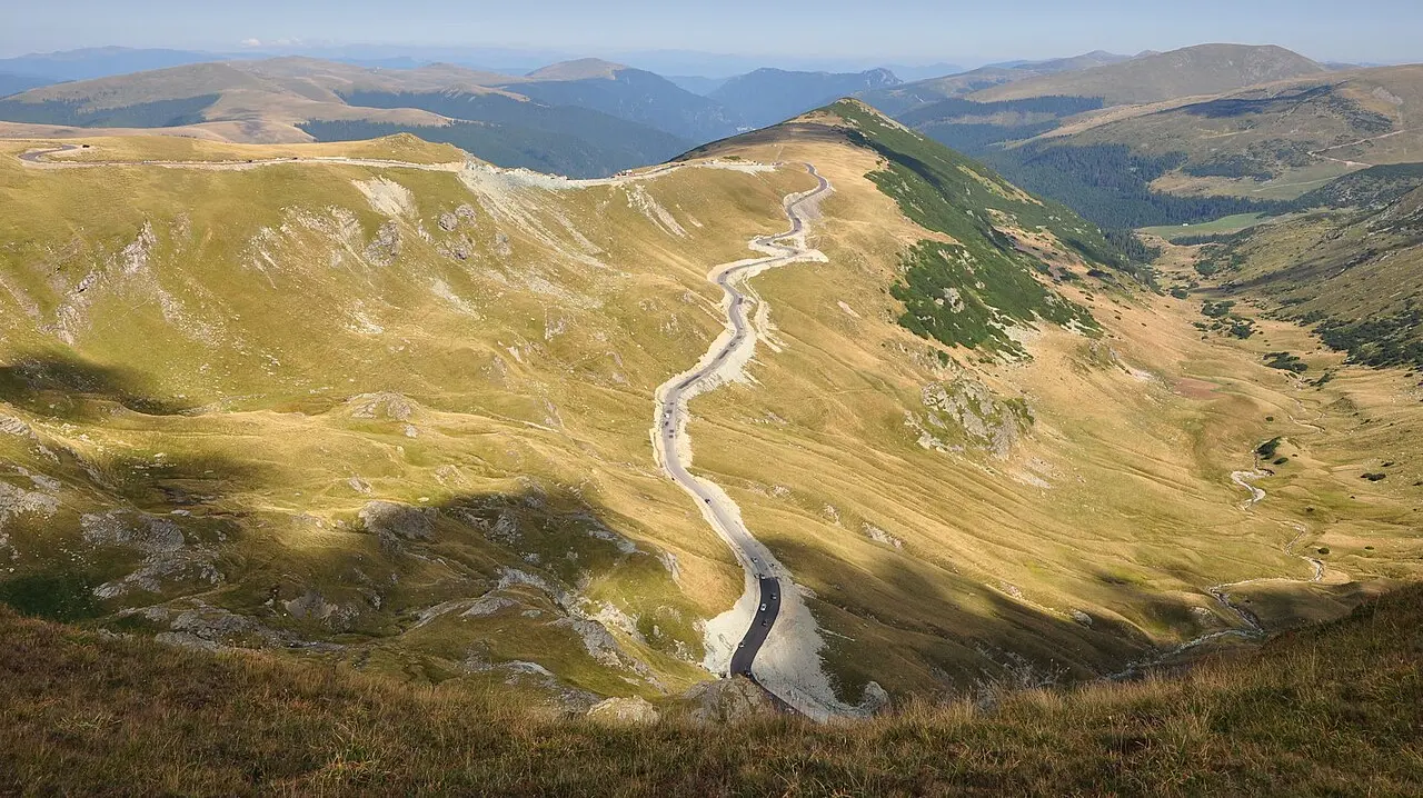 The DN67C Transalpina road climbing through green Parang Mountains under a wide summer sky