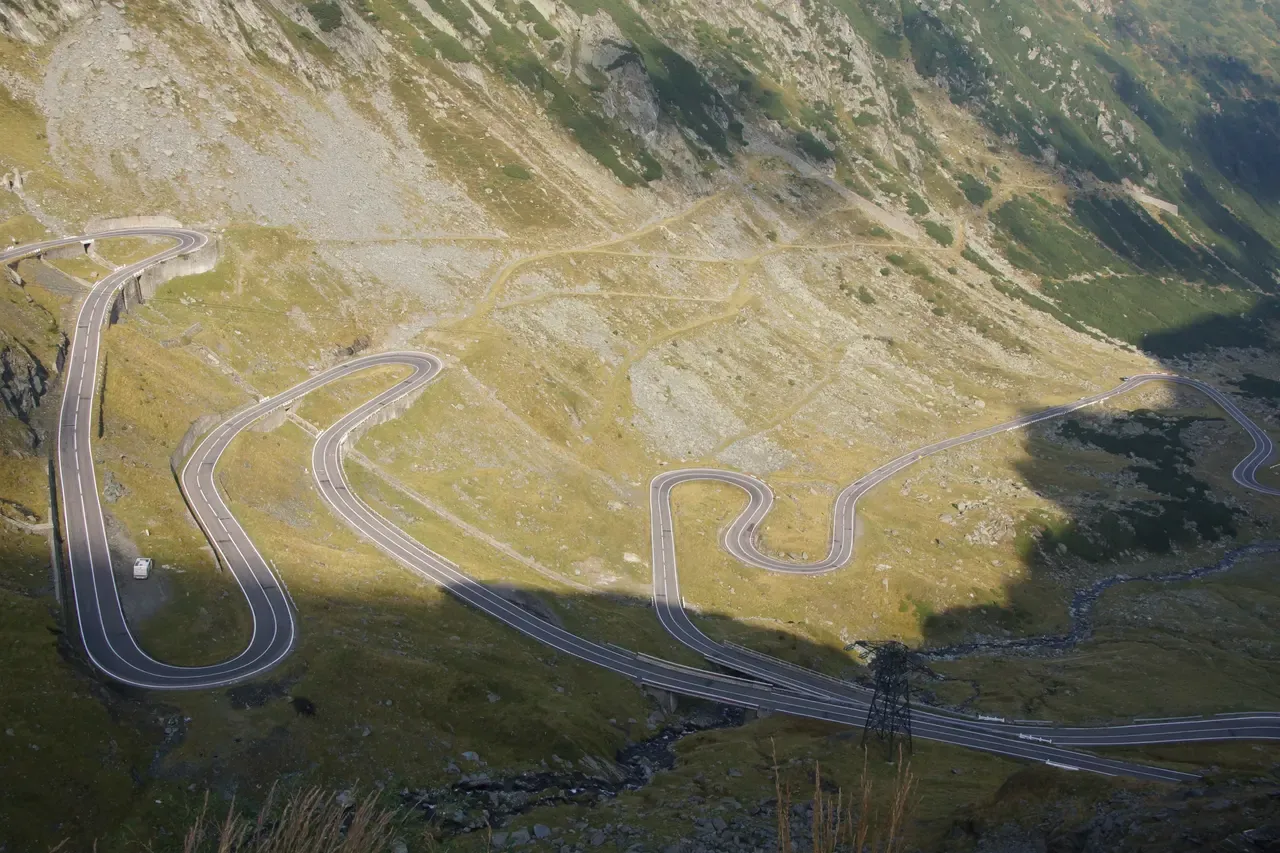 The hairpin switchbacks of the Transfagarasan road climbing a green mountainside, a camper van mid-corner