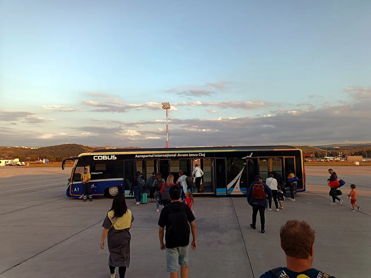 Passengers walking across the tarmac to board a Cobus apron transfer bus at Cluj Avram Iancu International Airport at dusk