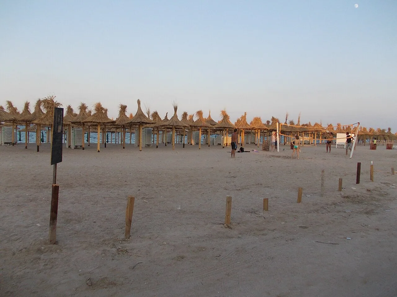 A wide view of Vama Veche's beach, low guesthouses and awnings lining the sand and the Black Sea stretching to the horizon