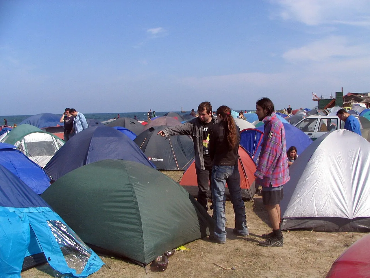 Rows of colourful tents pitched close together on the sand at Vama Veche, with the Black Sea visible behind them