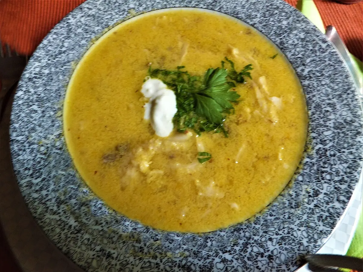 A bowl of creamy golden ciorba soup topped with a spoon of sour cream and chopped parsley