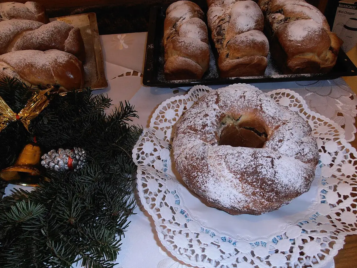 A ring of cozonac sweet bread dusted with sugar beside loaf cozonacs and Christmas greenery