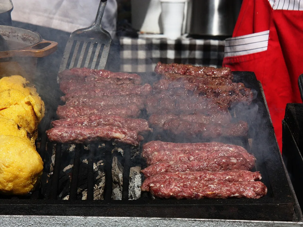 Rows of mici grilling over charcoal with smoke rising, a scoop of polenta on the side