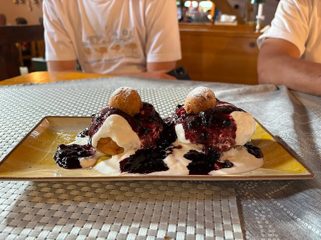 Two papanasi cheese doughnuts topped with sour cream and dark berry jam, a small dough ball on each