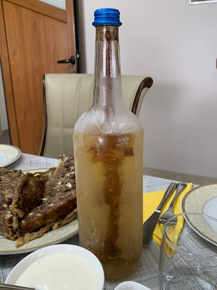 A frosted bottle of homemade tuica plum brandy on a table set for a meal