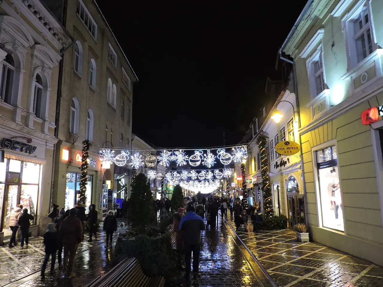 Strada Republicii, the pedestrian shopping street in Brasov old town, busy with people under festive lights in the evening