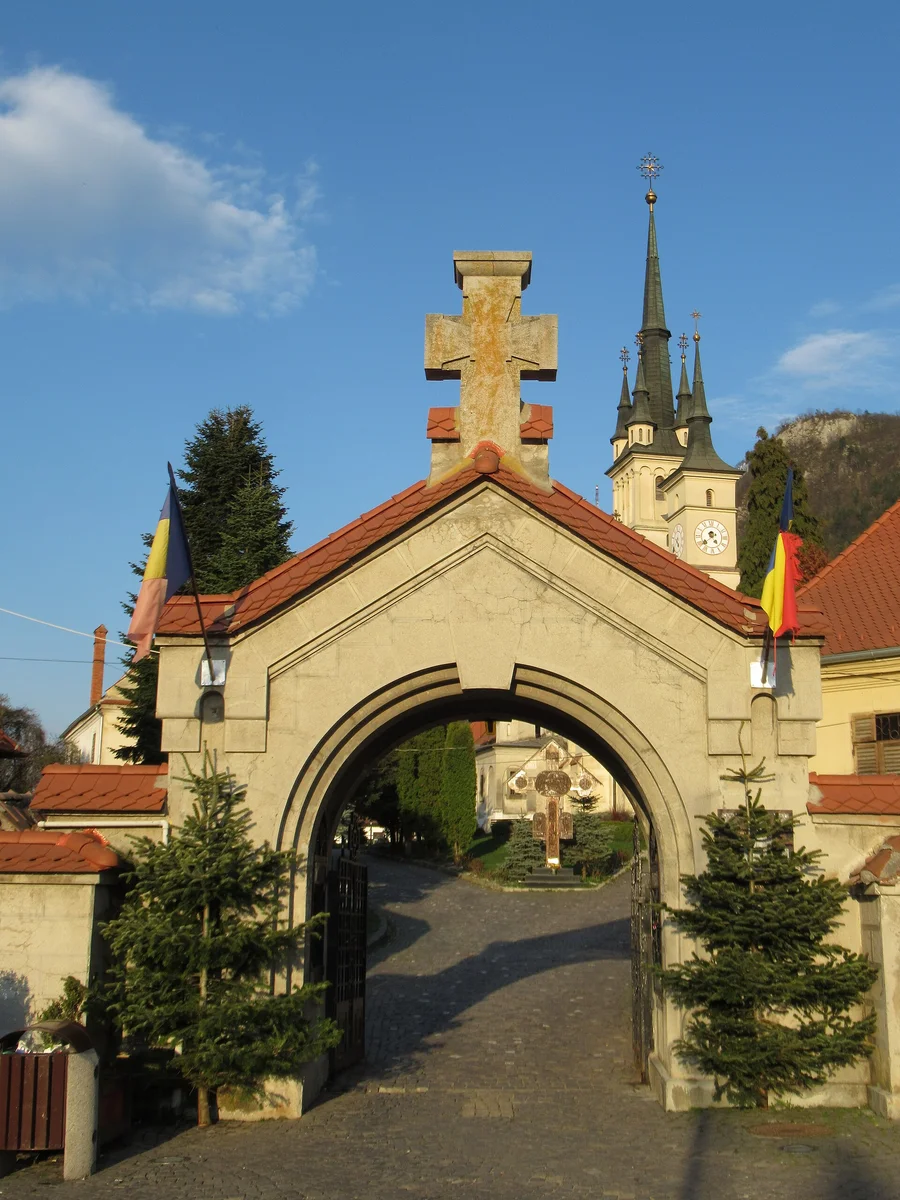 The stone gateway with a cross leading to St Nicholas Church in the Schei quarter of Brasov, its dark spires rising against a hill in golden light