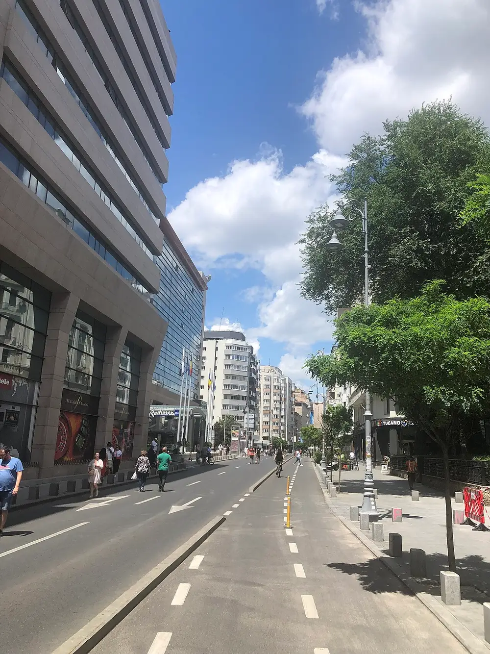 Calea Victoriei by day in Bucharest with a cycle lane, plane trees and the Radisson hotel frontage, people crossing the wide street