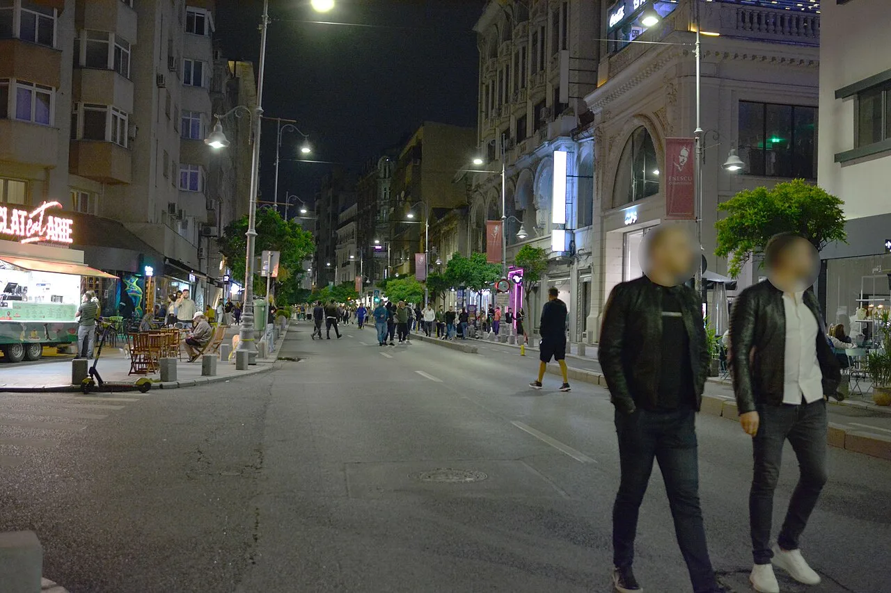 People strolling and cafe terraces along the pedestrianized Calea Victoriei in Bucharest at dusk, lit Belle Epoque buildings behind