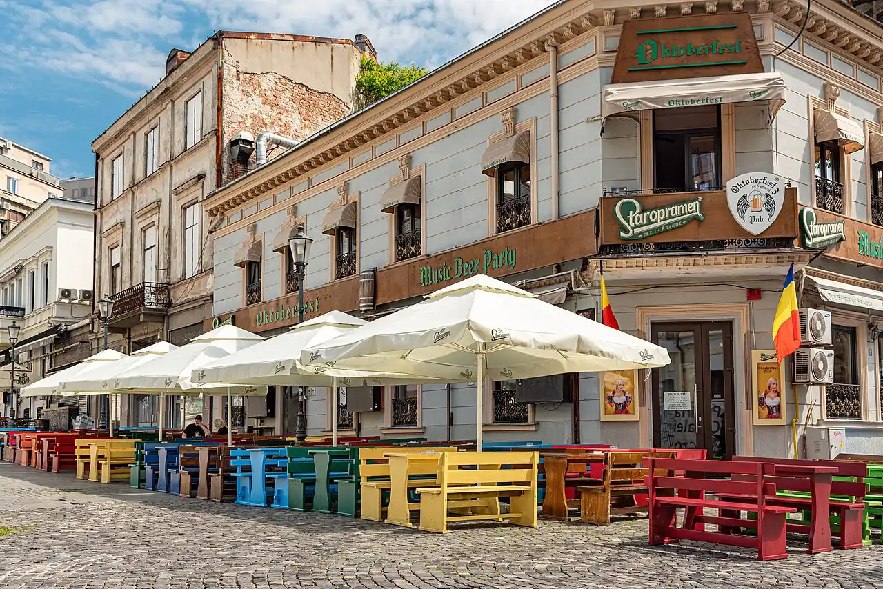 Cafe terraces with parasols packed along a pedestrian lane in the Lipscani Old Town of Bucharest, restored 19th-century facades on both sides