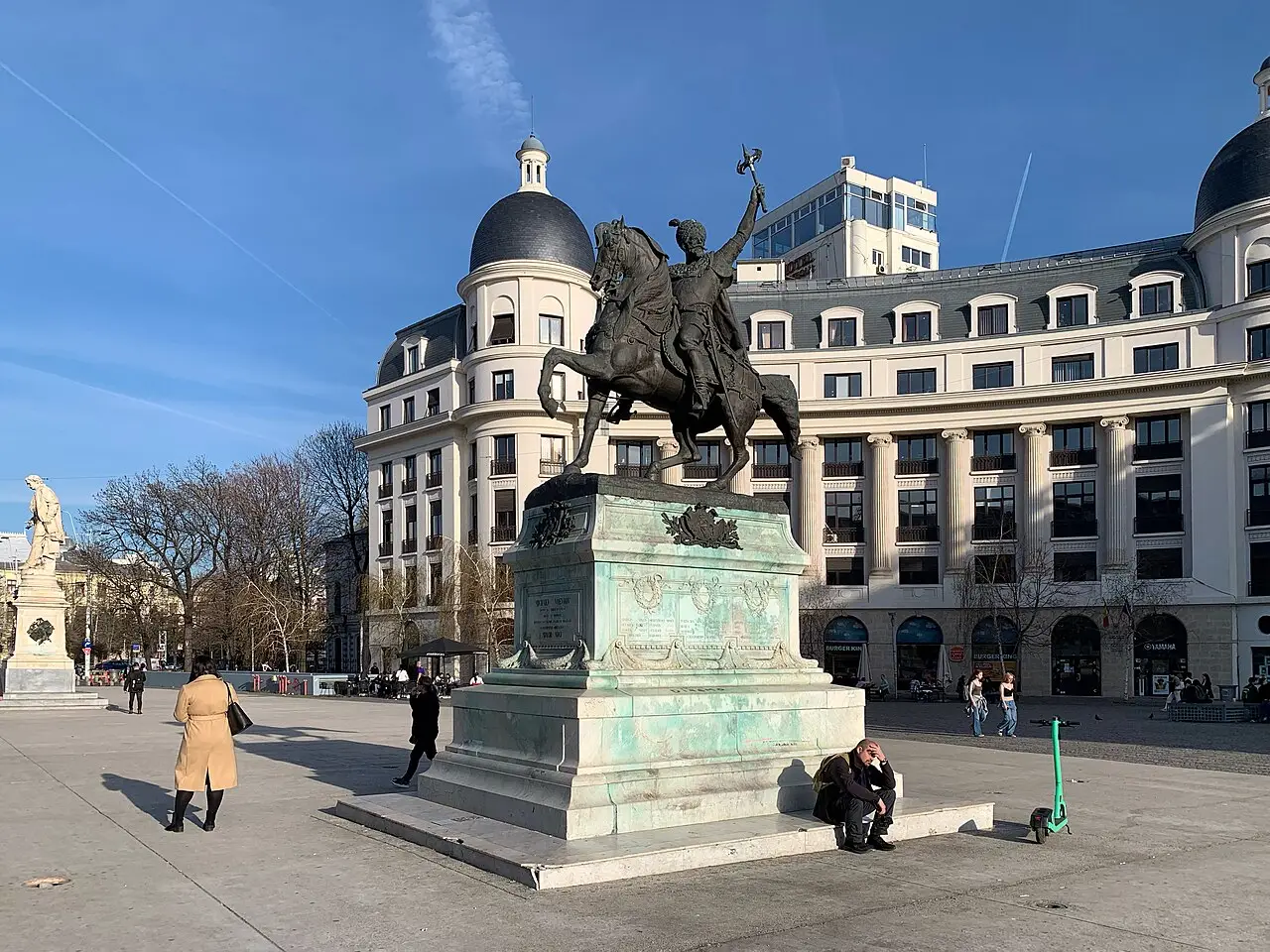 The equestrian statue of Mihai Viteazul on University Square in Bucharest under a blue sky, the University of Bucharest building behind