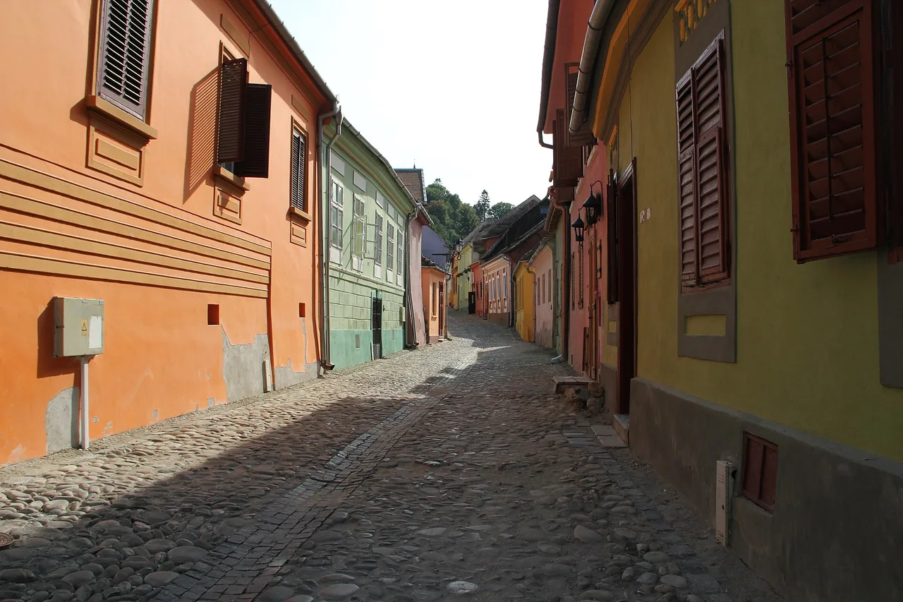 A narrow cobbled lane inside the Sighisoara citadel lined with pastel townhouses and flower boxes