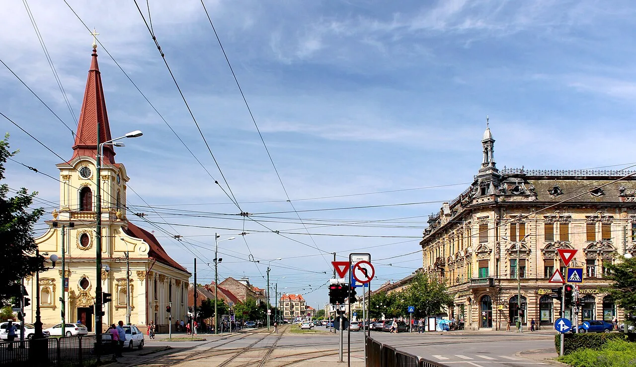 A parish church and an ornate Secession-style corner building facing each other across a tram-lined street in Iosefin, Timisoara